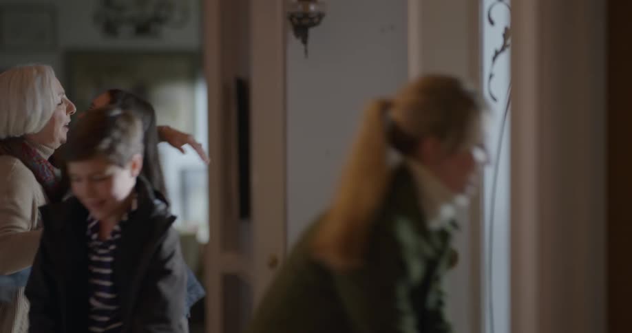 A woman happily opens a door to her house to greet the family on the other side with hugs