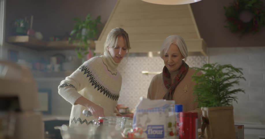 Two women are measuring ingredients and cooking together in a home kitchen