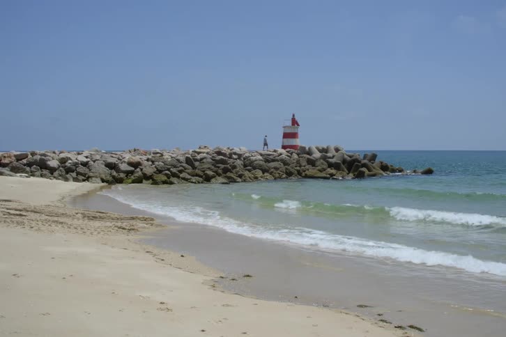 Waves gently wash upon a sandy beach as two people enjoy the scenery