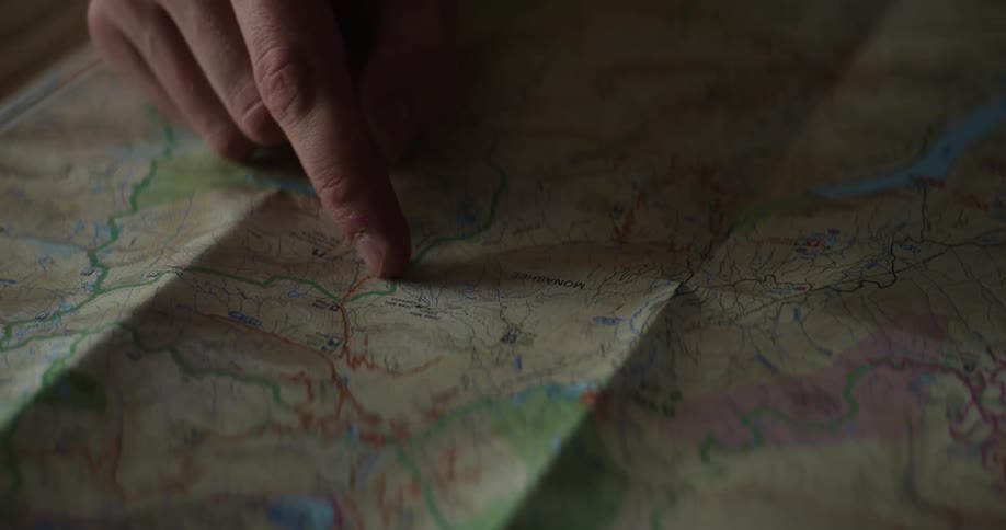 A person points at a location on an printed map that has been folded