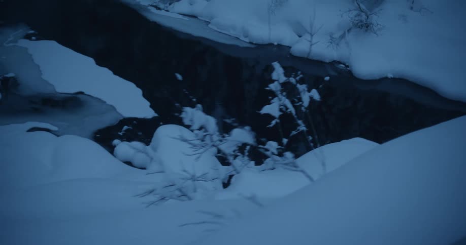 Snow surrounds the stream at sunset