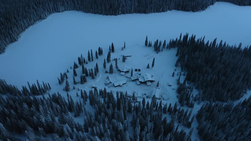 A group of remote buildings are covered in snow and surrounded by forest