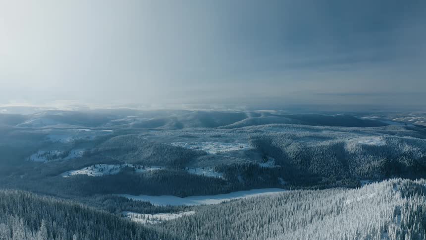 A snow covered mountain range slopes downward into a valley