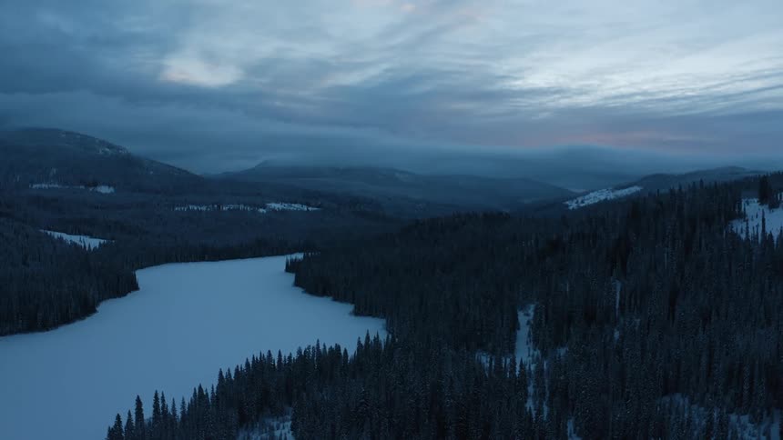 Forests cover a mountain range that surrounds a snow covered valley