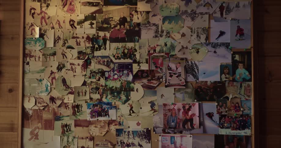 Corkboard full of pinned photographs rests against wall made of wooden boards