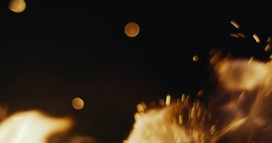 A burning fire releases sparks and embers into the darkness of night