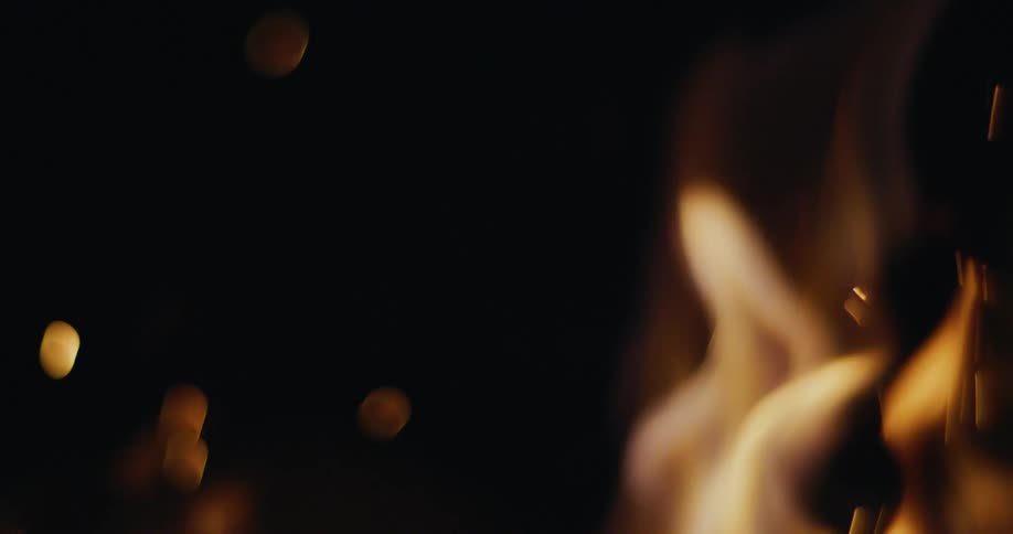 Orange flames create sparks and floating spots of light against a black background