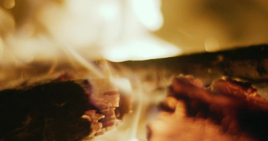 Flames flicker and release embers as fire burns a piece of wood