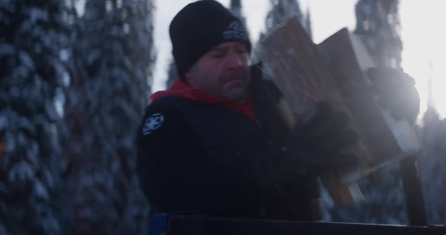 A man carries an armful of firewood while outdoors in the snow