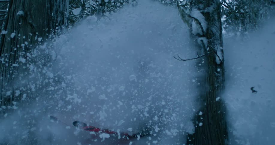 Snow flies as a skier holds his ski poles and slides sideways down a forest mountain hill moving between trees