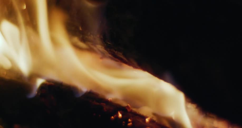 Flames burn brightly and release embers as a piece of wood burns