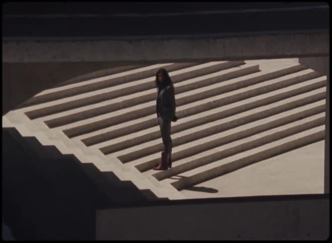 Person with long hair wearing a suit standing on a staircase stirring something