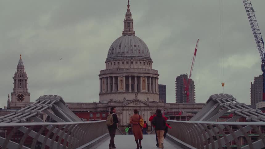 Group of people walking on a walkway atop a building heading towards a round tower building on a cloudy day