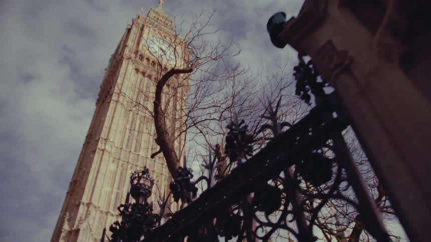 A clock tower on a high rise building by a intricate wrought iron fence