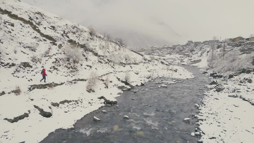 A person is hiking through the snow by the stream