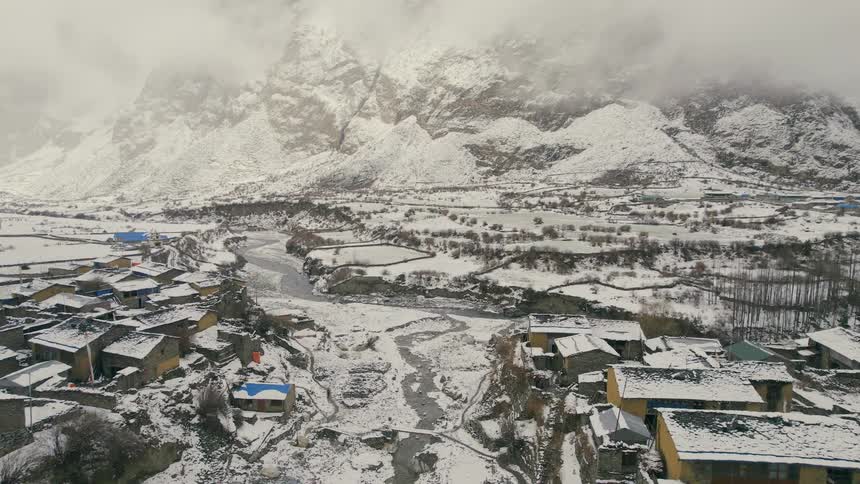 Streams and river wind through snow covered town near mountain on cloudy day