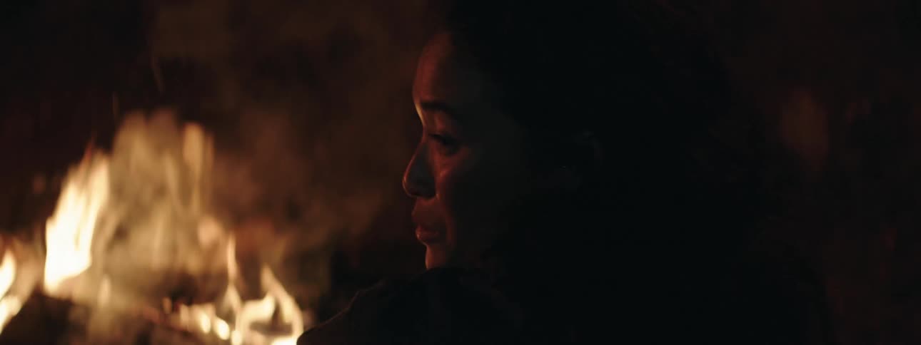 Woman sitting by bonfire talks to person