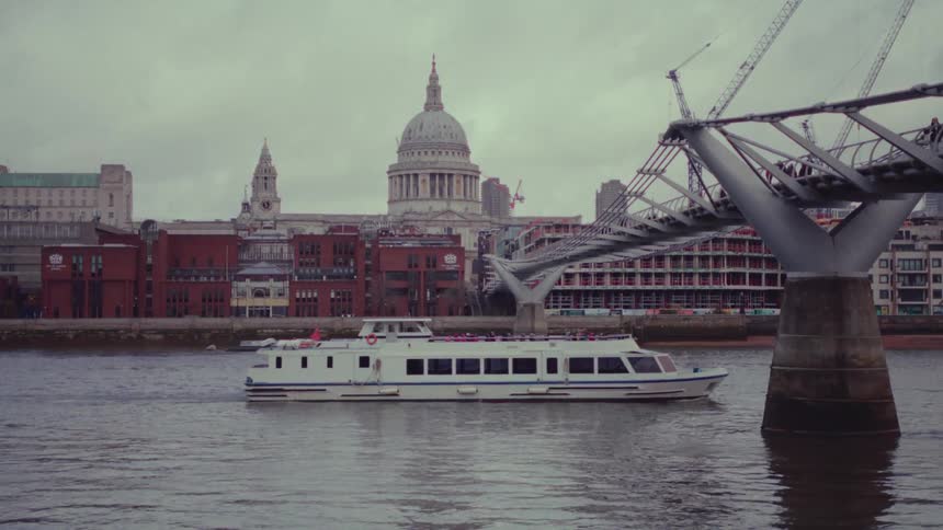 Ferry sailing under the millennium bridge across river thames in london