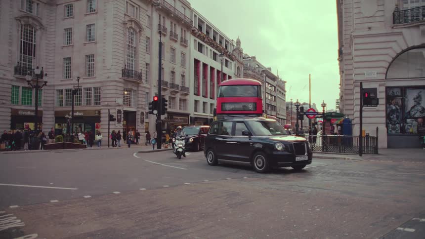 The bustling street is filled with the sight of red london buses and cars driving along creating a vibrant and lively scene in the city