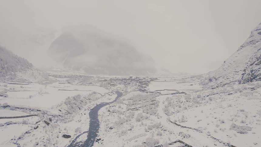 The stunning aerial view reveals a river meandering through a snowy valley with majestic mountains shrouded in fog