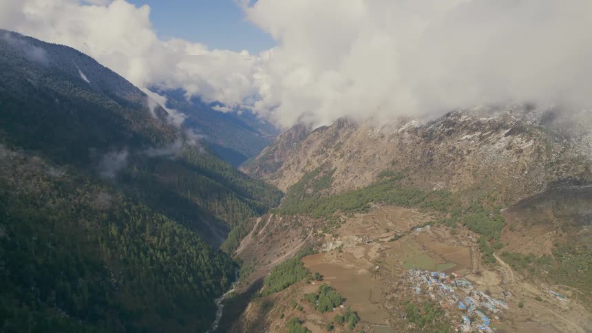 Clouds cover the mountain tops above a river running through a deep valley