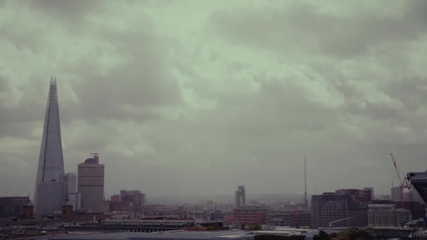 A tall pyramidal building under construction in the city on an overcast day