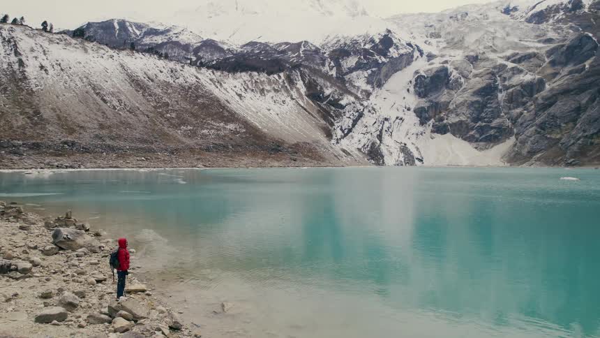 A person standing on the edge of a turquoise lake surrounded by mountains and hillsides