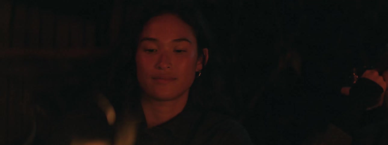 A young woman sits by the campfire while drinking a bottle of beer