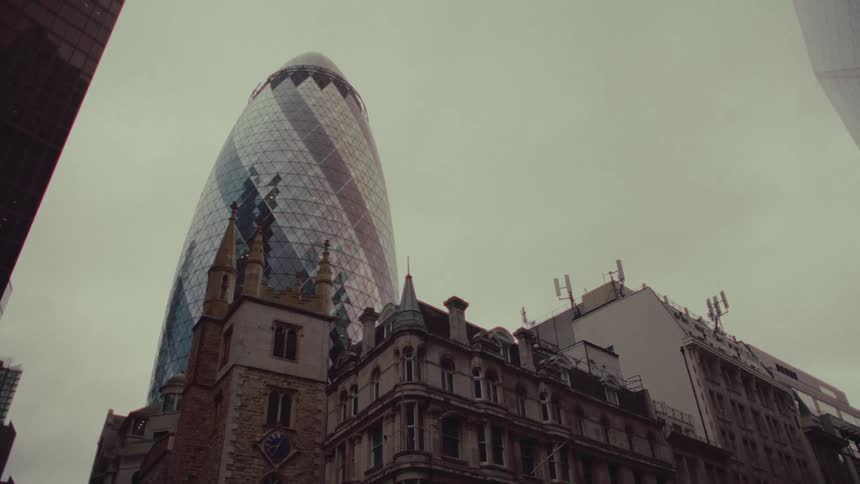 The gherkin building in london towers over other buildings under a cloudy sky