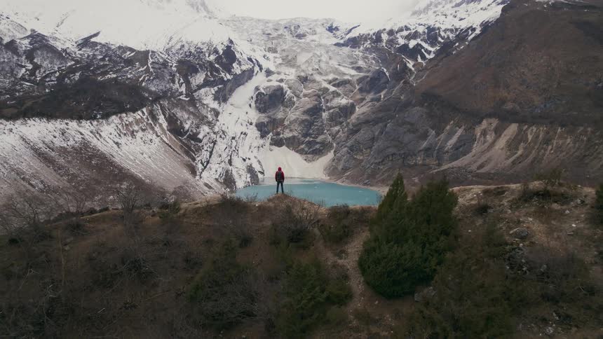 A man stands on a mountain overlooking a lake in between a mountain range
