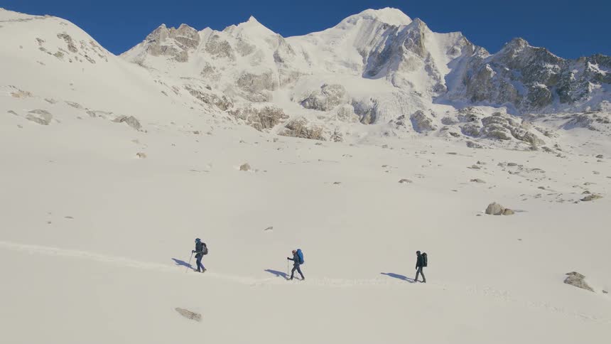 A group of mountaineers hike up a snowy mountain slope during the day