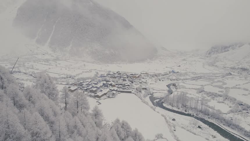 Aerial view of snowy mountain slope a town in a valley and a distant mountain ridge in fog