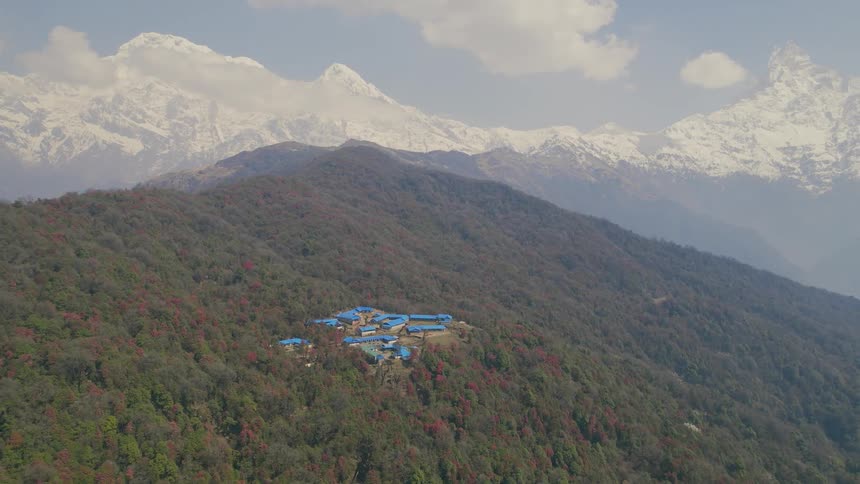 Several buildings situated in a highland area surrounded by lush green vegetation while majestic mountains visible in the background