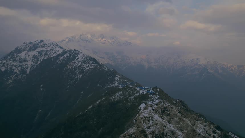 Light snow covers a mountain ridge high in the clouds at dusk