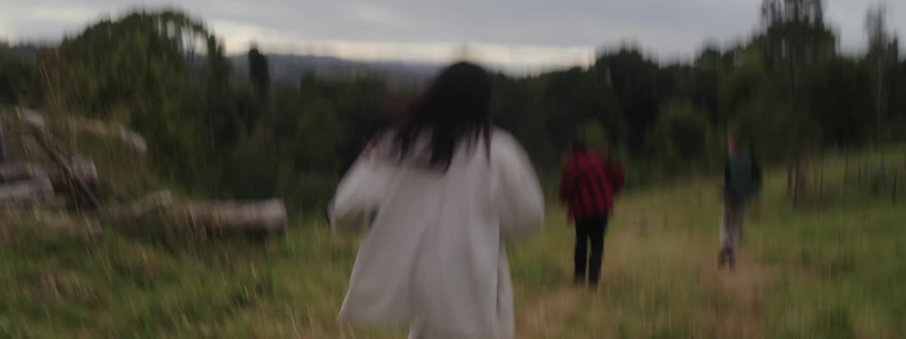A woman is running behind two people including a dog in a grassland