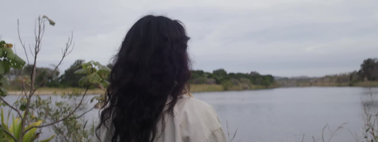 Woman stands on lake shore looking around on a cloudy day