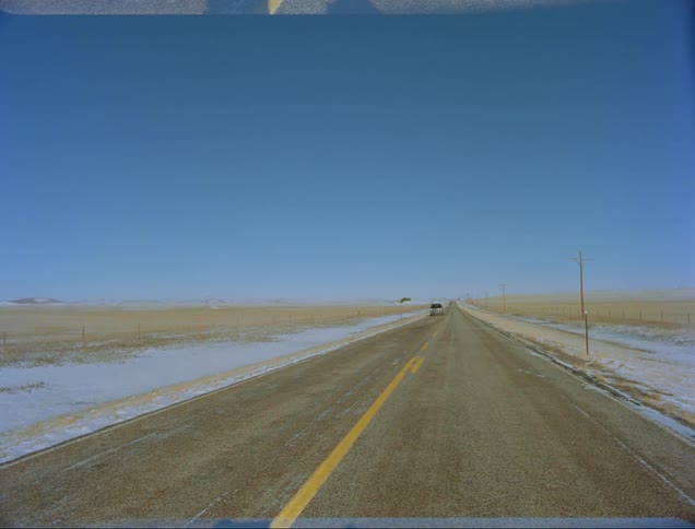 A vehicle driving on a road with the sky and clouds in the background