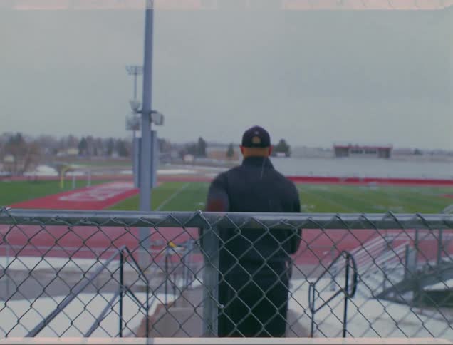 A man jumps over a chain link fence to access a track and football field