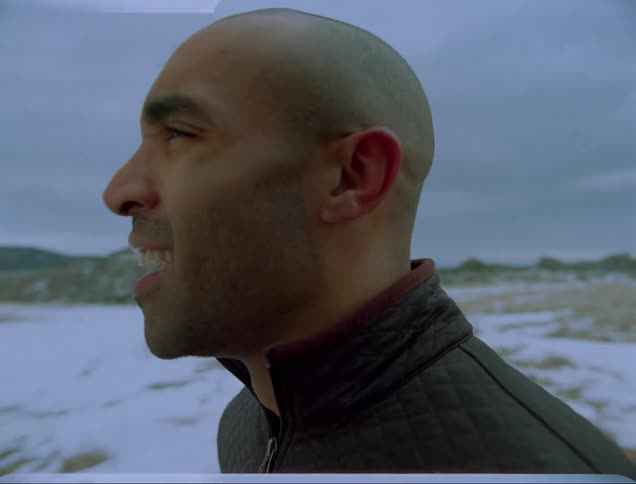 A man attempts to catch his breath while standing outdoors in a snowy field on a cloudy day