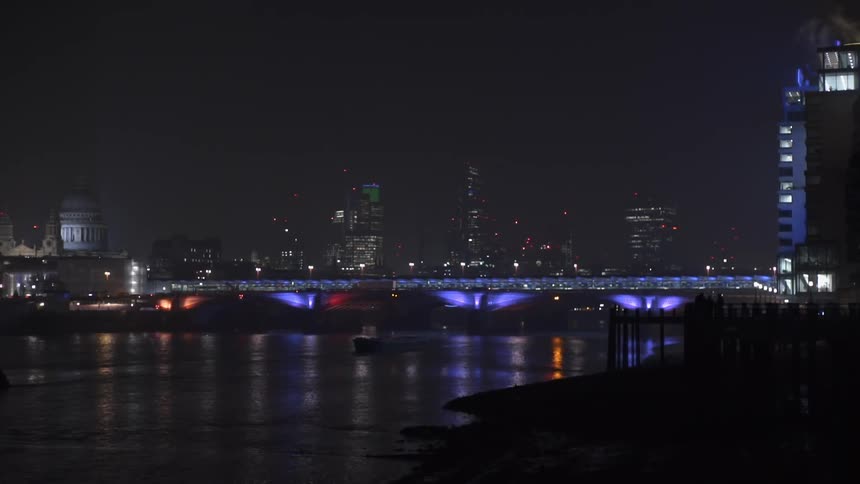 A boat moves up river beyond a bridge and city lit up at night