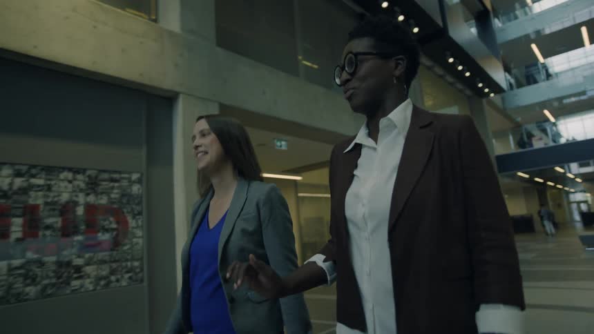 Two women walk together through the lobby of a large building