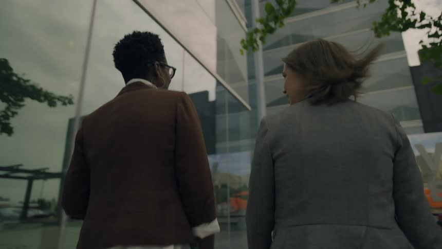 Two women talk while walking on a windy day near a modern building in the university