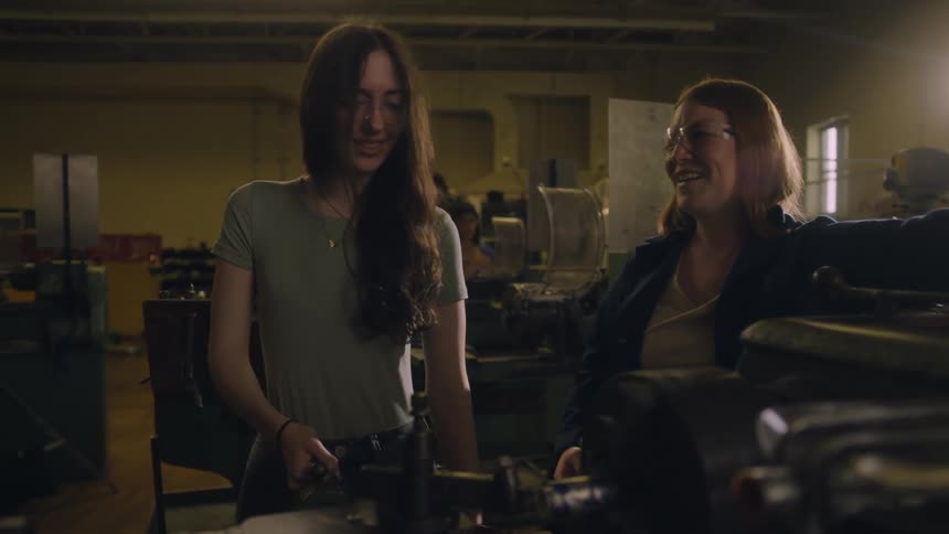 Two happy women working with a lathe in a workshop