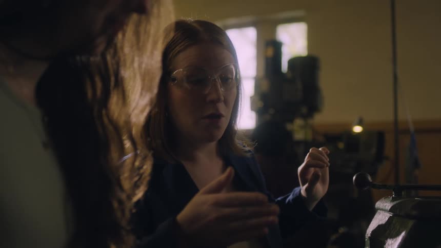 Woman teaches teenage girl how to use a machine in a factory setting