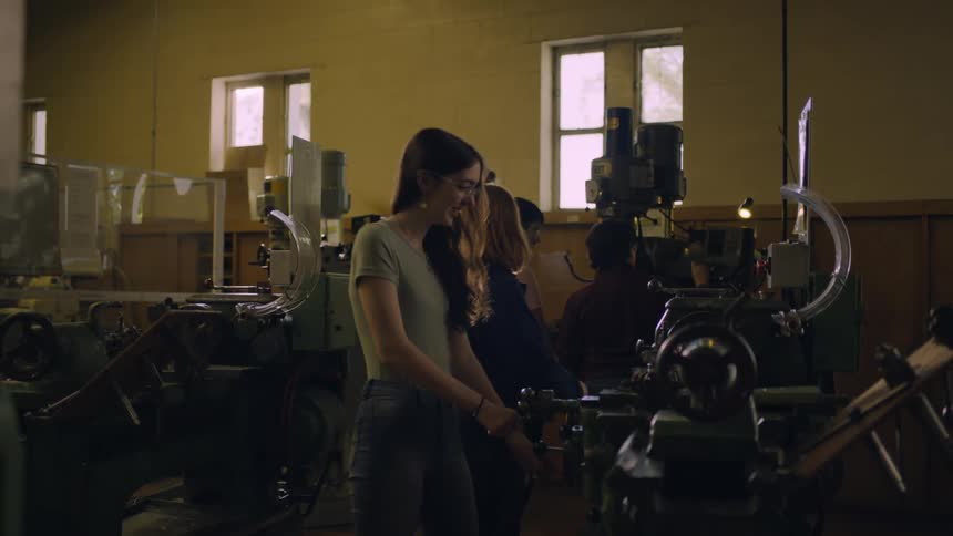 Teacher helps a student working on a lathe in the workshop