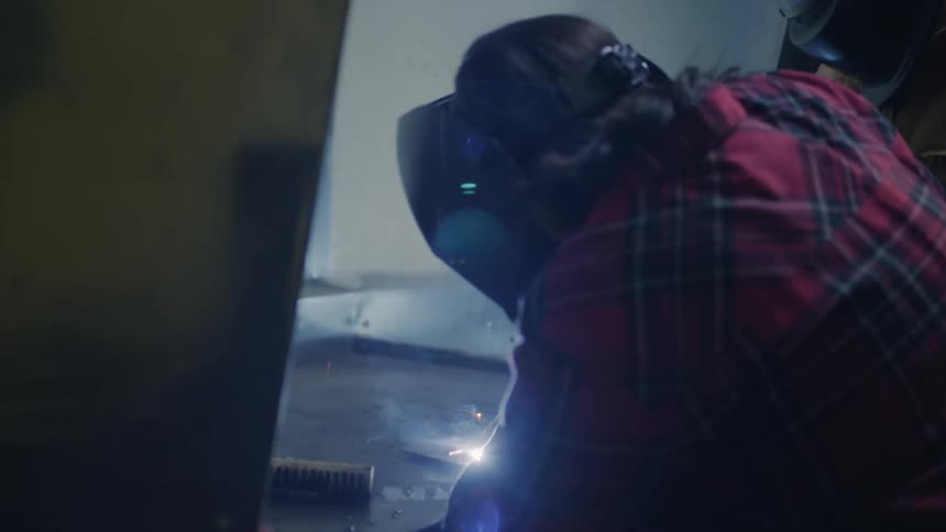 Two people putting on headgear in a welding workshop welding a piece of metal