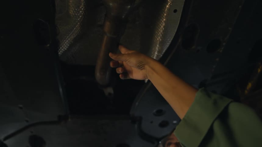 One mechanic gestures while talking to person that is also looking at metal connection