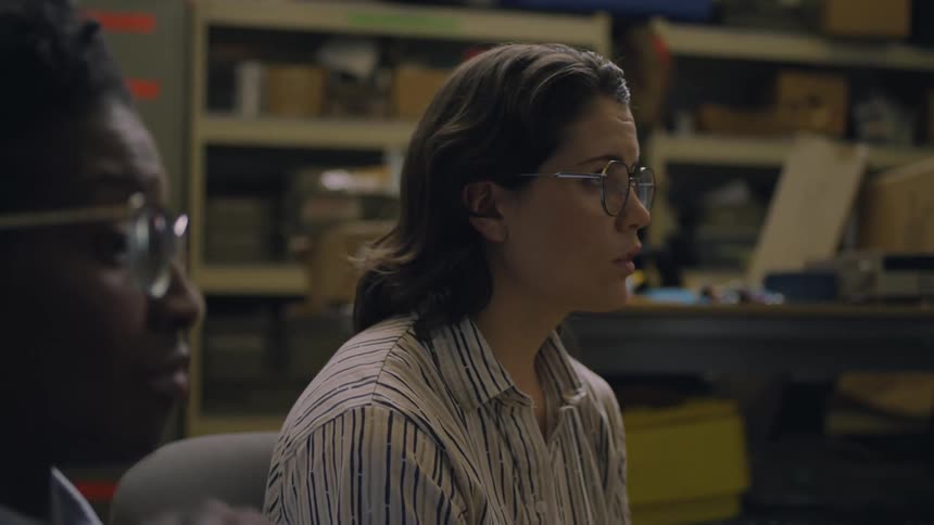 A black woman and a white woman seated near each other in a room both wearing glasses nodding their heads in mutual acknowledgement of the ongoing discussion