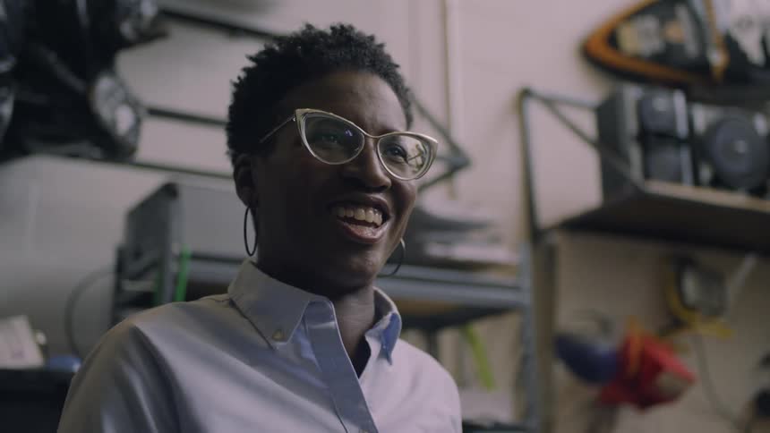 A woman smiles after leaning over to inspect a machine in a tech lab