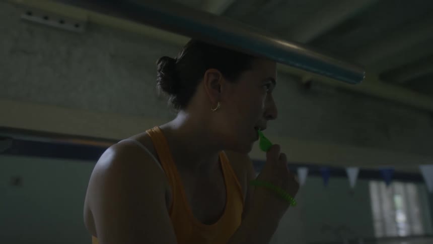 A woman in a swimsuit yells and blows a whistle while coaching others